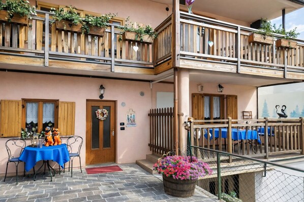 A two-story building with a balcony, a table with chairs, and a flower pot.
