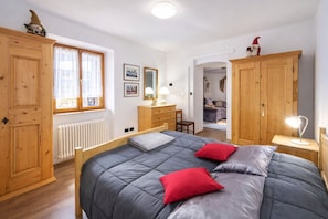 A bedroom with a large bed, wooden wardrobe, a desk with a lamp, and a window with curtains. - LA CANONICA nature and peace, with terrace Wi-Fi PetFriendly with dog area (Baselga di Piné)