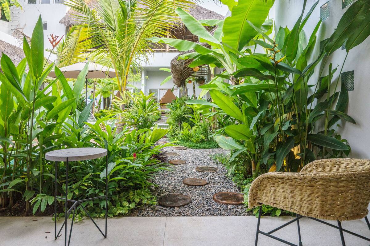 Un jardin avec un sentier, une chaise en osier et une petite table.