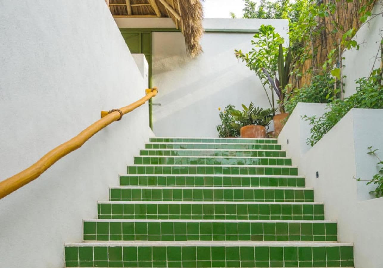 A staircase with green tiles, a wooden handrail, and potted plants.