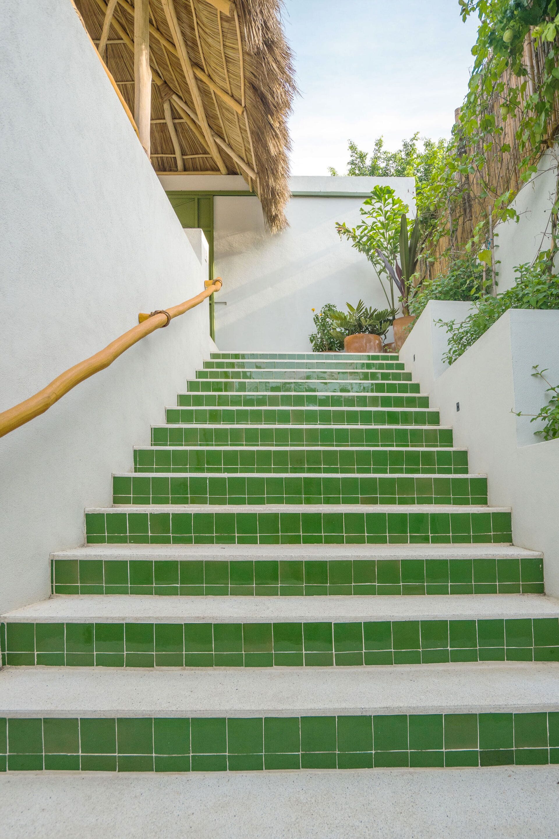 A staircase with green tiles leading up to a building with a thatched roof and a white wall.