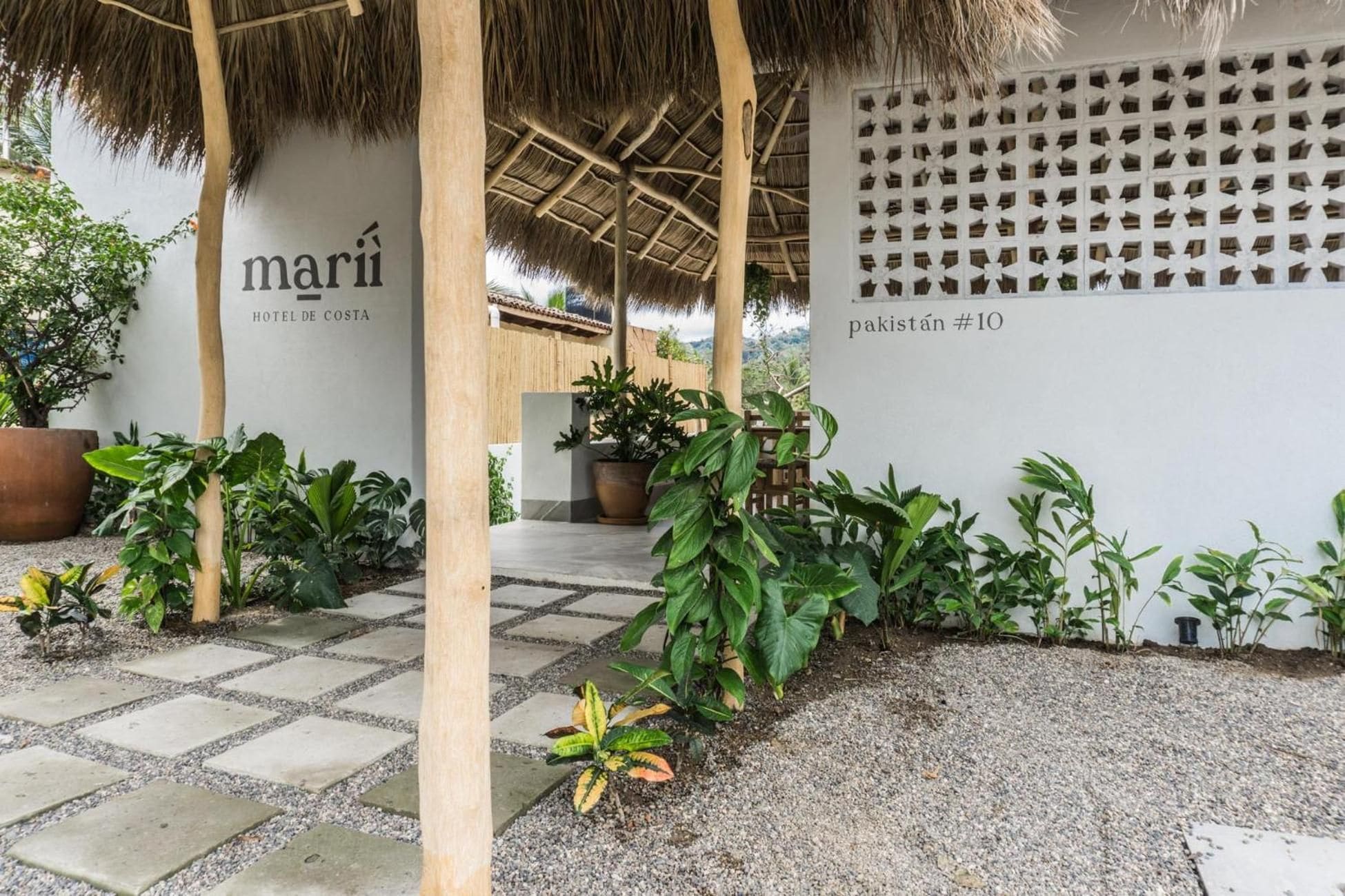 A hotel entrance with a thatched roof, potted plants, and a wall with a geometric pattern.