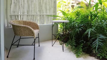 Rincón con una silla de mimbre y una pequeña mesa redonda, rodeado de exuberantes plantas verdes.