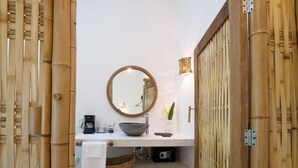 A bathroom with a round mirror, a bowl sink, a towel, a coffee maker, and a small basket.
