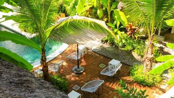 A patio area with a pool, white chairs, and tropical plants.
