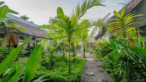 A tropical garden pathway leading to a thatched-roof building with lush greenery and a clear sky.