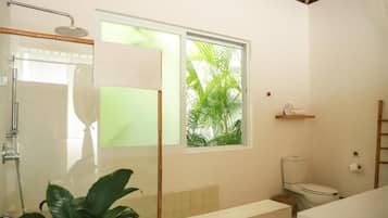 Un bagno con doccia, WC e una finestra vista verde.