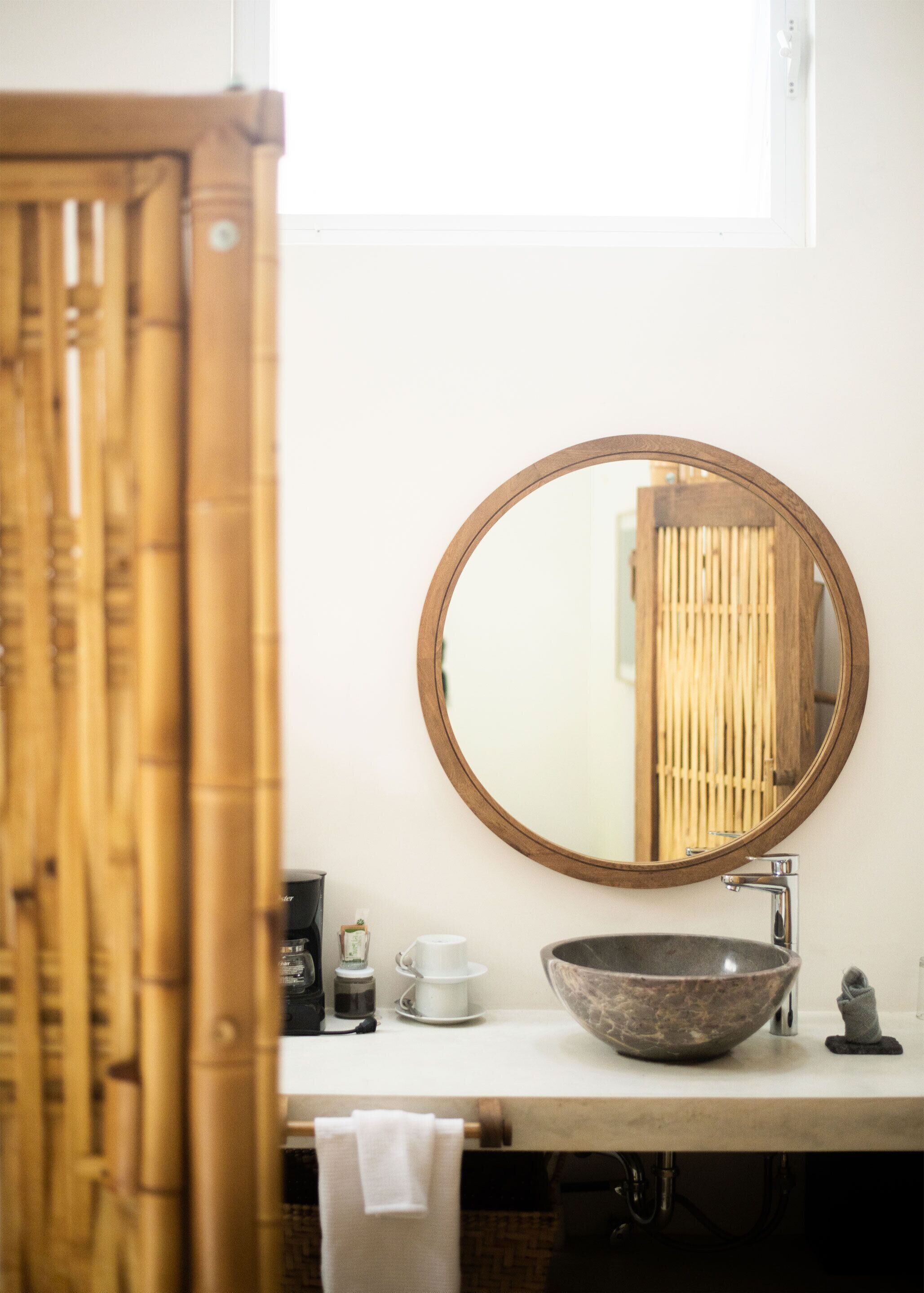A bathroom with a round mirror, a sink, and a bamboo curtain.