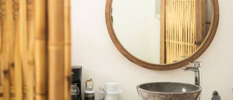 A bathroom with a round mirror, a sink, and a bamboo curtain.
