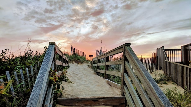 A wooden boardwalk leading to a beach with a sunset in the background. - Charming Cottage, South Nags Head, 5 min walk to the beach (Nags Head)