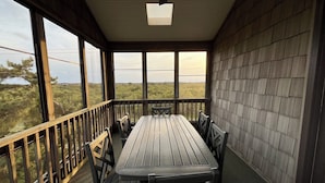 A covered outdoor area with a wooden table and chairs, large windows, and a view of the landscape. - Charming Cottage, South Nags Head, 5 min walk to the beach (Nags Head)