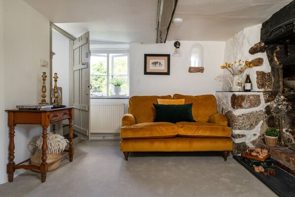 A room with a sofa, a wooden table, a stone wall, and a window with a view of greenery.