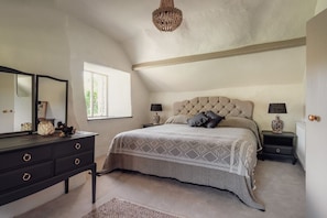 Quarto com cama grande, cômoda, duas mesas de cabeceira com luminárias, lustre e janela.
