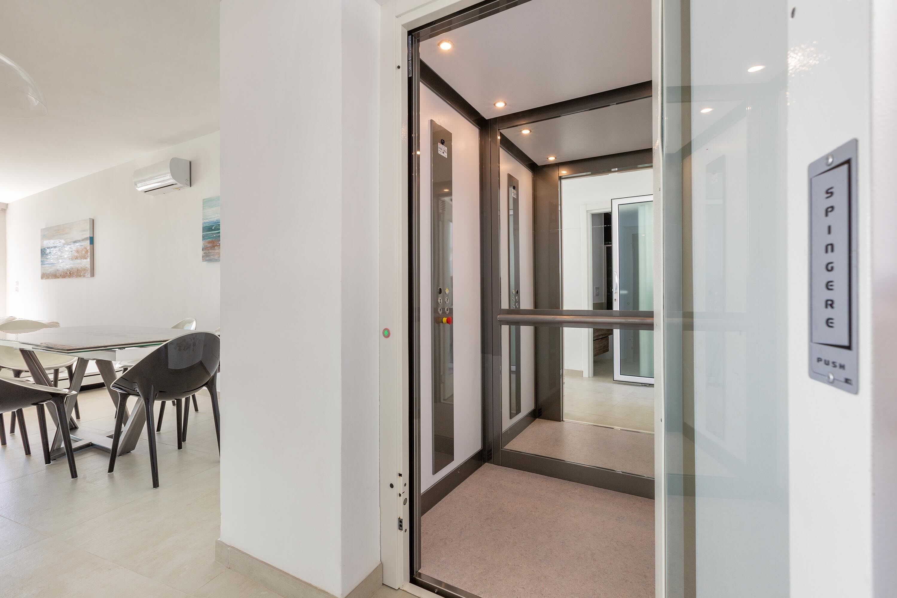 Een modern interieur met een glazen liften, een eethoek met tafel en stoelen, en een bordje aan de muur.