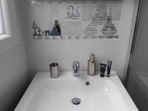 Casa de banho com lavatório branco, espelho e artigos de higiene, incluindo um frasco de loção.
