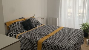 Makuuhuone, jossa on sänky, patteri, ikkuna, jossa on verhot, ja katosta roikkuva valaisin.