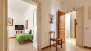 Una habitación con una cama, una silla, un televisor y una puerta que da a otra estancia.