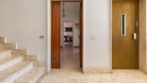 Un pasillo con una escalera de mármol, una puerta de madera y una cocina visible a través de un vano abierto.