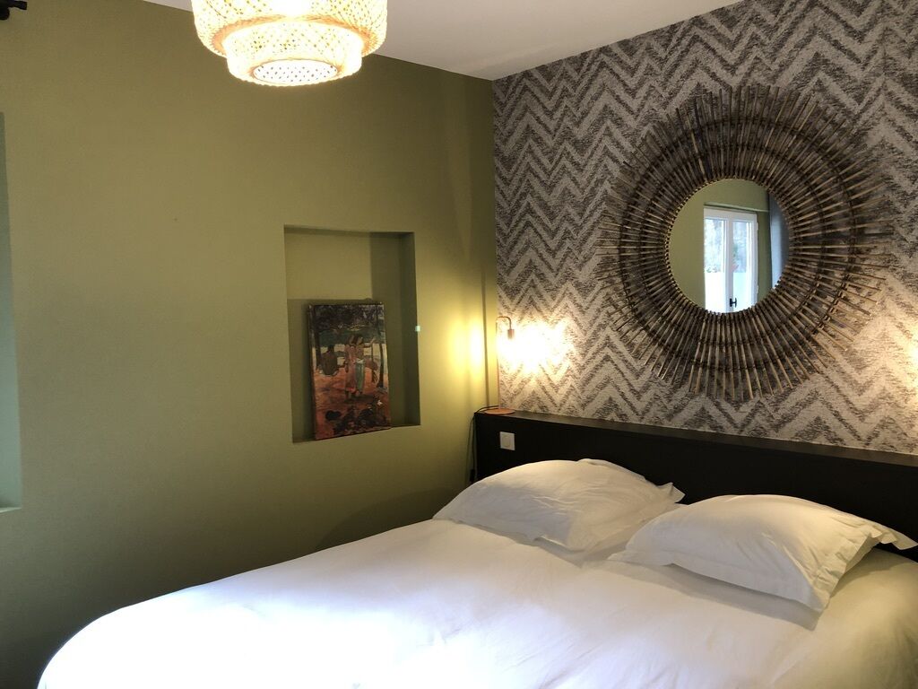 A bedroom with a bed, a wall-mounted mirror, and a painting.
