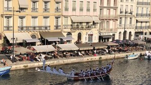 A traditional boat with rowers, docked near a waterfront with buildings and outdoor seating areas.