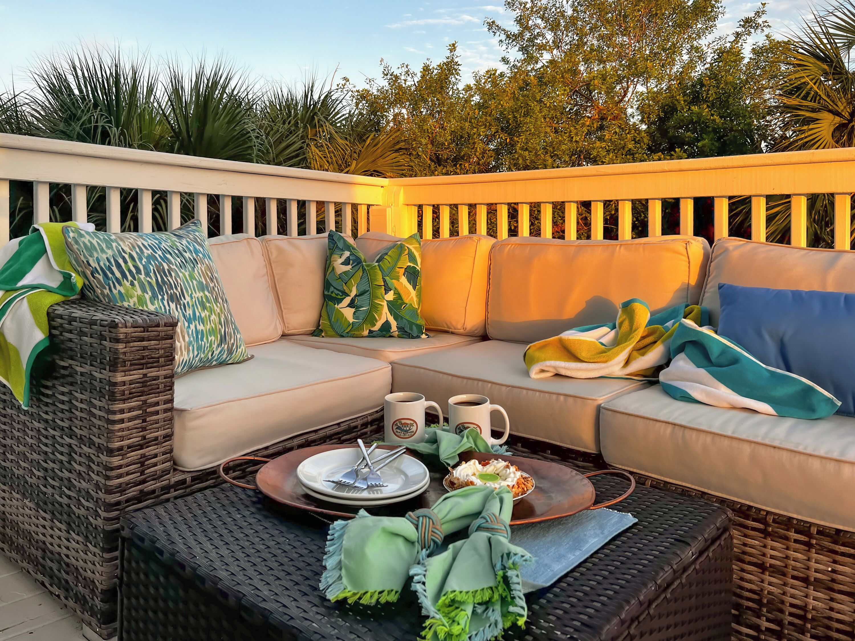 A wicker sofa with cushions, a tray with a plate and utensils, and a mug on a woven table.