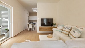 A modern living room with a flat-screen TV, a sofa, and a dining area in the background. - La Giada by Perle di Puglia (Maruggio)