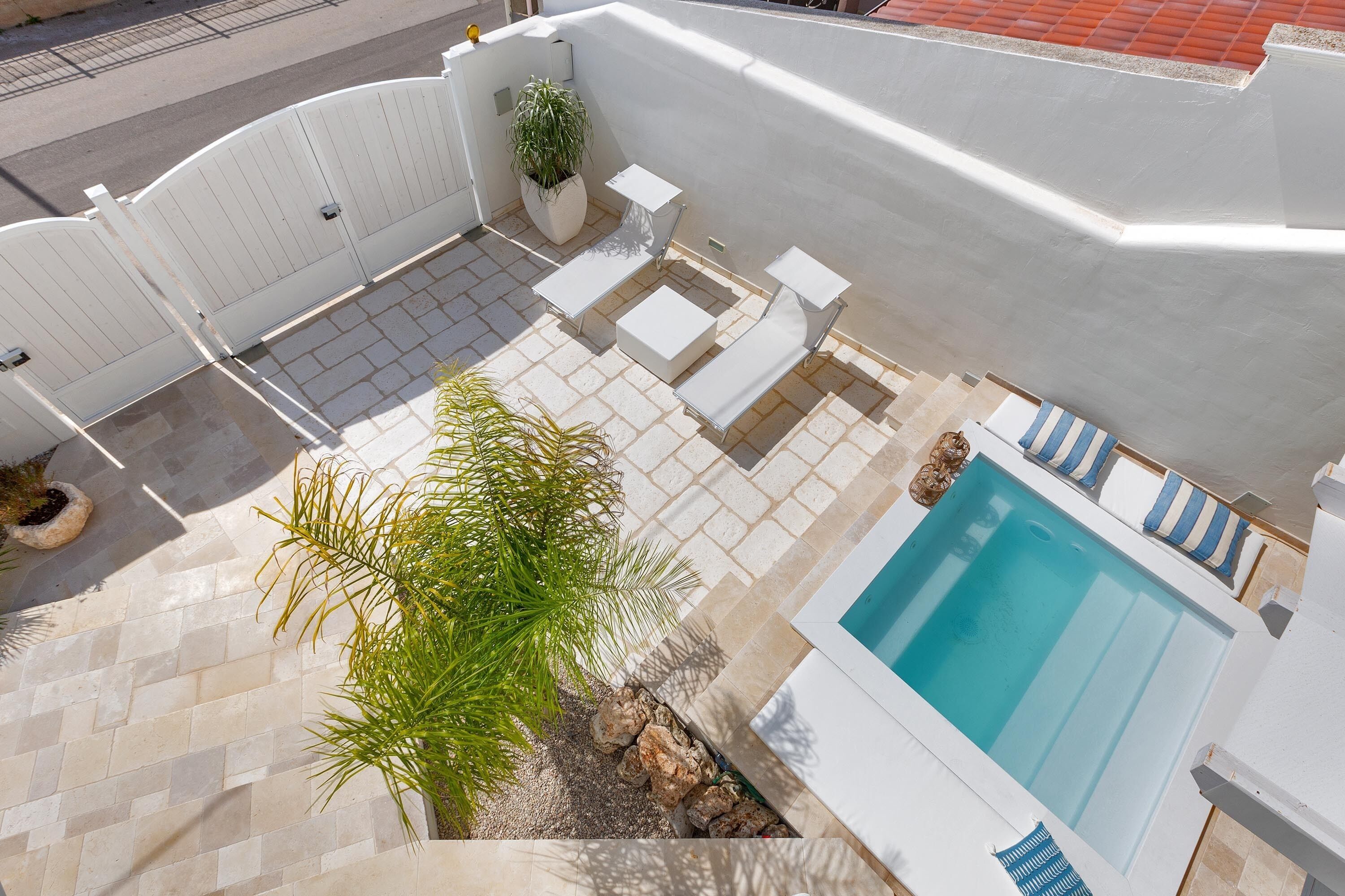 A rooftop pool area with a hot tub, lounge chairs, and a potted plant.