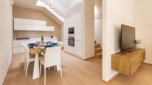 A modern kitchen with white cabinetry, a dining table with chairs, a built-in oven, and a TV on a wooden console. - La Giada by Perle di Puglia (Maruggio)