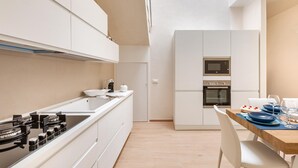 A modern kitchen with white cabinets, a wooden dining table, and a built-in oven. - La Giada by Perle di Puglia (Maruggio)