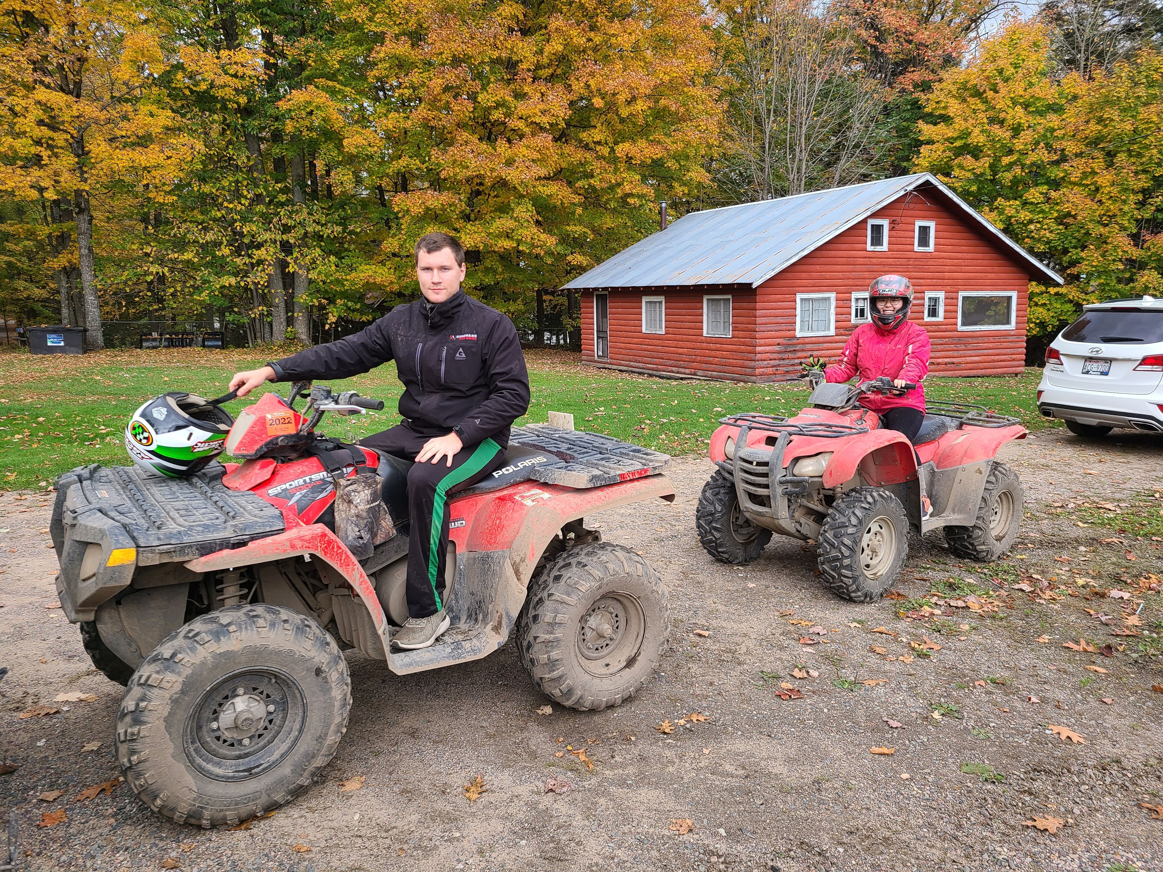 Zwei Personen fahren mit Quads vor einem roten Haus.