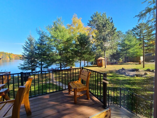 Relax on the lakeside deck surrounded by lush greenery and trees, with a serene view of the calm lake and dock in the distance.