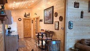 Un intérieur de chalet chaleureux avec un coin repas en bois, une cuisine équipée d’une machine à café et un espace de vie comprenant un canapé et une petite table d’appoint.