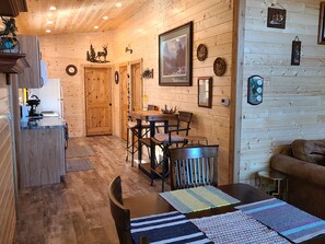 Cozy cabin with a rustic interior, featuring a dining area with a wooden table and chairs, a side table, and a cushioned bench.