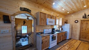 L’intérieur d’une cabane en bois comprend un coin cuisine équipé de meubles en bois, d’un four à micro-ondes, d’une cuisinière et d’un réfrigérateur.