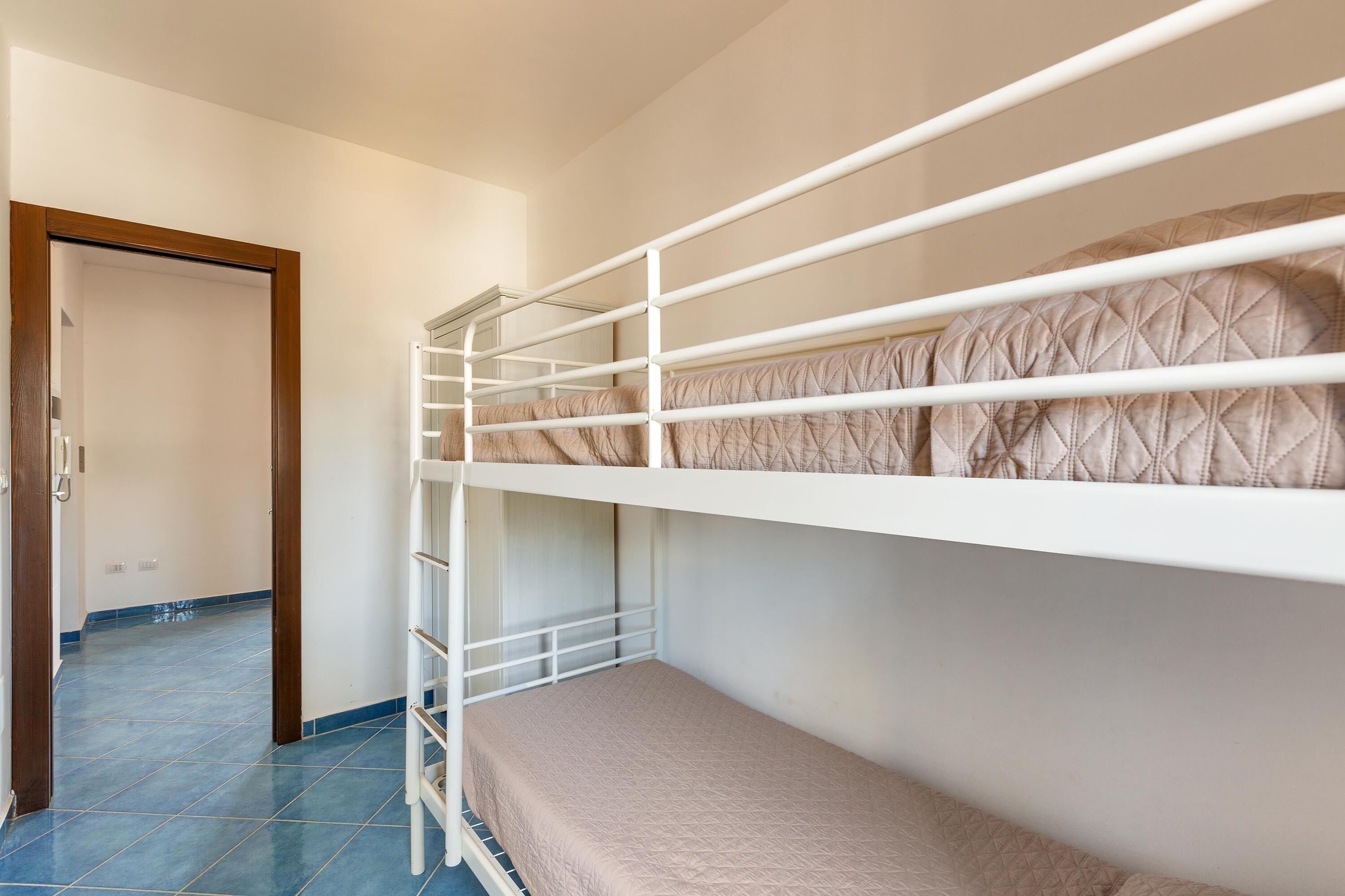 Habitación con literas, puerta de madera y suelo de baldosas azules.