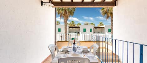 An outdoor dining area with a table set for four, surrounded by white chairs, under a wooden pergola.
