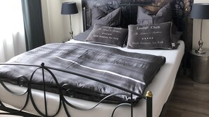 Een moderne slaapkamer met een groot bed, een zwart metalen frame, grijze beddengoed en een grote wandtapijt.