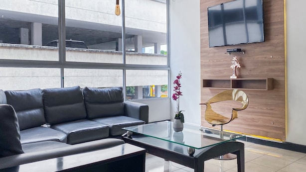 Un salon moderne avec un canapé gris, une table basse en verre et un téléviseur fixé à un mur en bois.