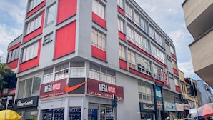 Un immeuble à plusieurs étages, doté d’une façade rouge et grise bien visible, sur laquelle on peut lire les inscriptions « Mega Outlet » et « Hôtel ».
