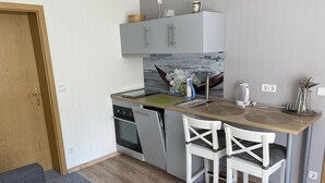 Una cocina compacta con horno integrado, un lavamanos y un pequeño comedor con dos sillas blancas.
