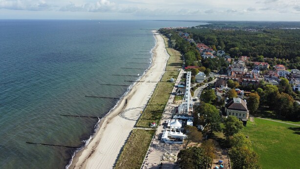 Vista aérea de un pueblo costero con una extensa playa de arena, un paseo marítimo y edificios residenciales.