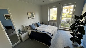Un dormitorio con cama, mesitas de noche, un radiador, una ventana y vistas al exterior.