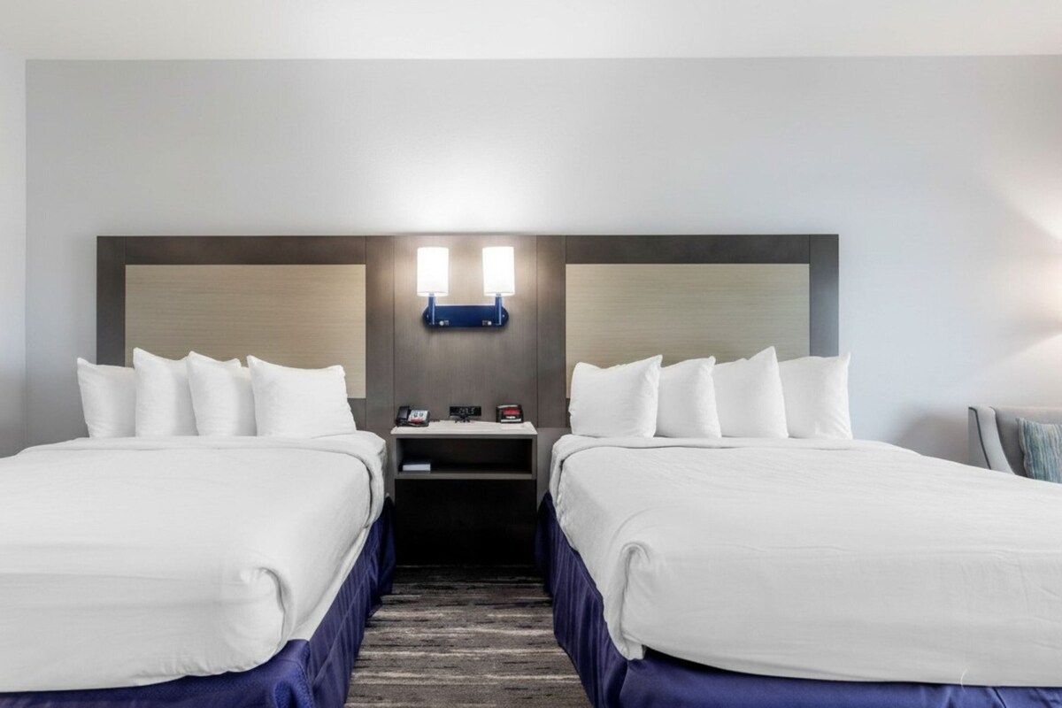 Habitación de hotel con dos camas, una mesita de noche, una lámpara fijada a la pared y un cuadro enmarcado.