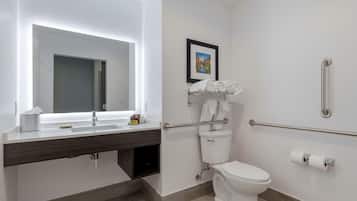 A modern bathroom with a white sink, mirror, and toilet. There are handrails for accessibility, a towel rack, and a framed picture on the wall.