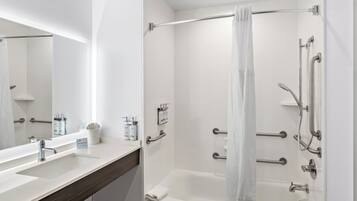 Une salle de bain moderne équipée d’une baignoire, d’une douche et d’un meuble-lavabo avec un miroir et des articles de toilette.