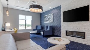 Ein moderner Lounge-Bereich mit einer Couch, Sesseln, einem Couchtisch, einem Kamin und einem großen, an der Wand befestigten Fernseher.