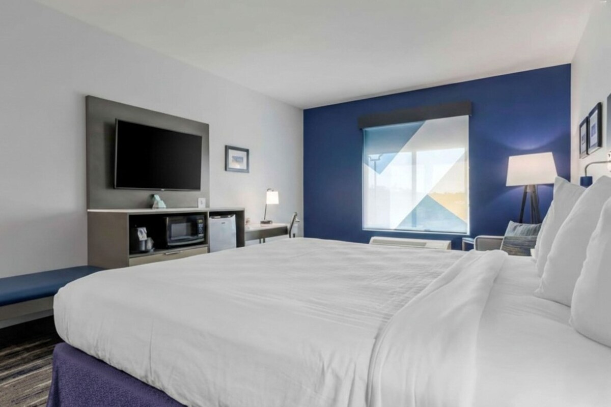 Habitación de hotel con una cama grande, televisión de pantalla plana, escritorio con computadora y ventana con vista.