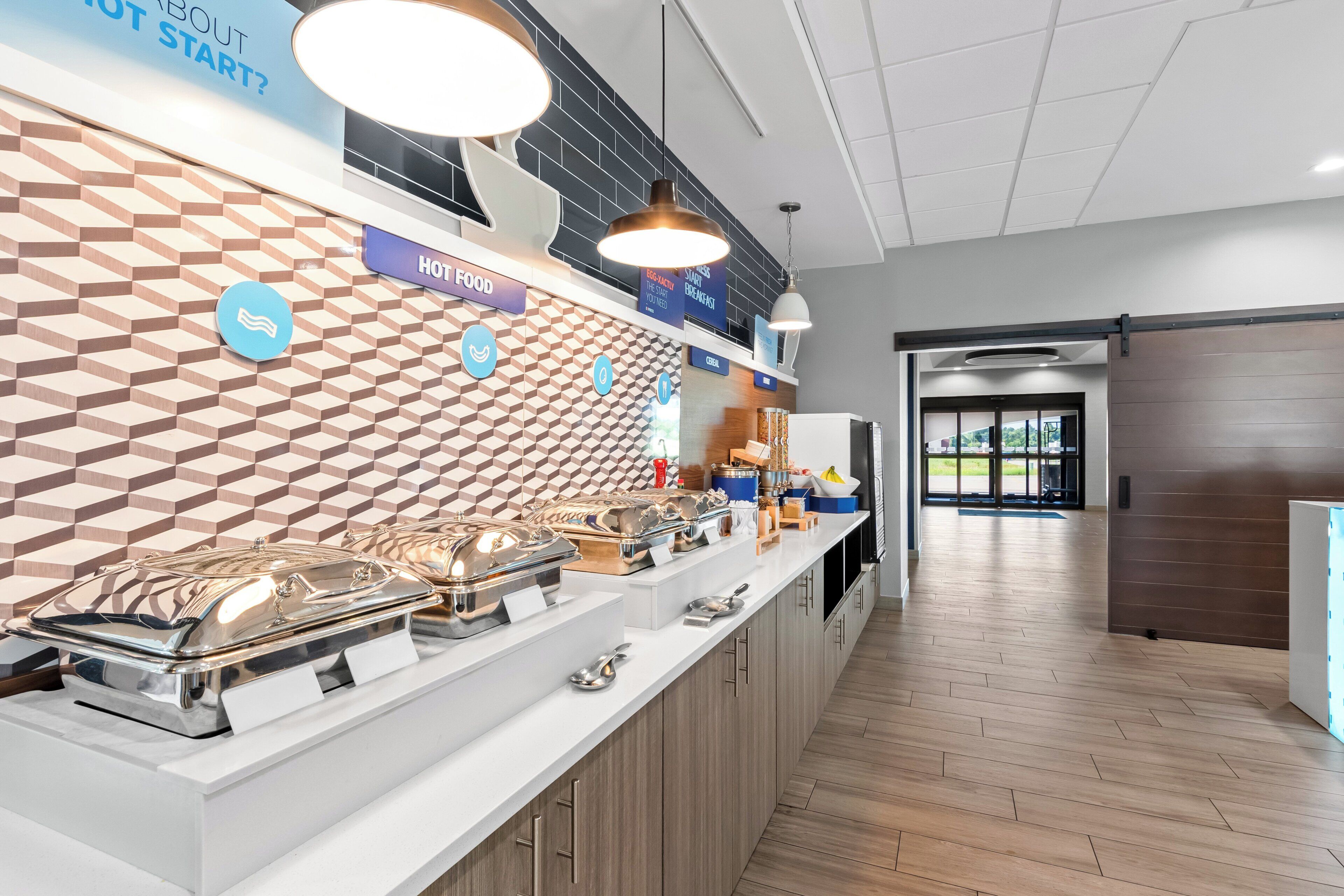 Espaço de buffet de café da manhã com diversas opções de comida, design moderno com azulejos geométricos na parede e ambiente limpo e bem iluminado.