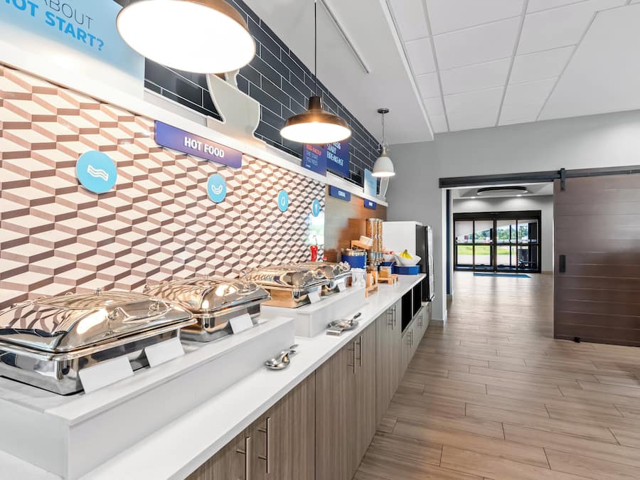 A breakfast buffet area with a variety of food options, a modern design with geometric wall tiles, and a clean, well-lit environment.