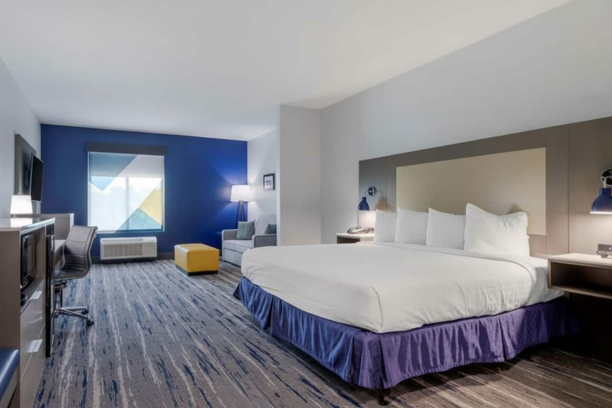 Une chambre d’hôtel avec un grand lit, un bureau avec une chaise, un canapé, une petite table avec une lampe et un téléviseur.